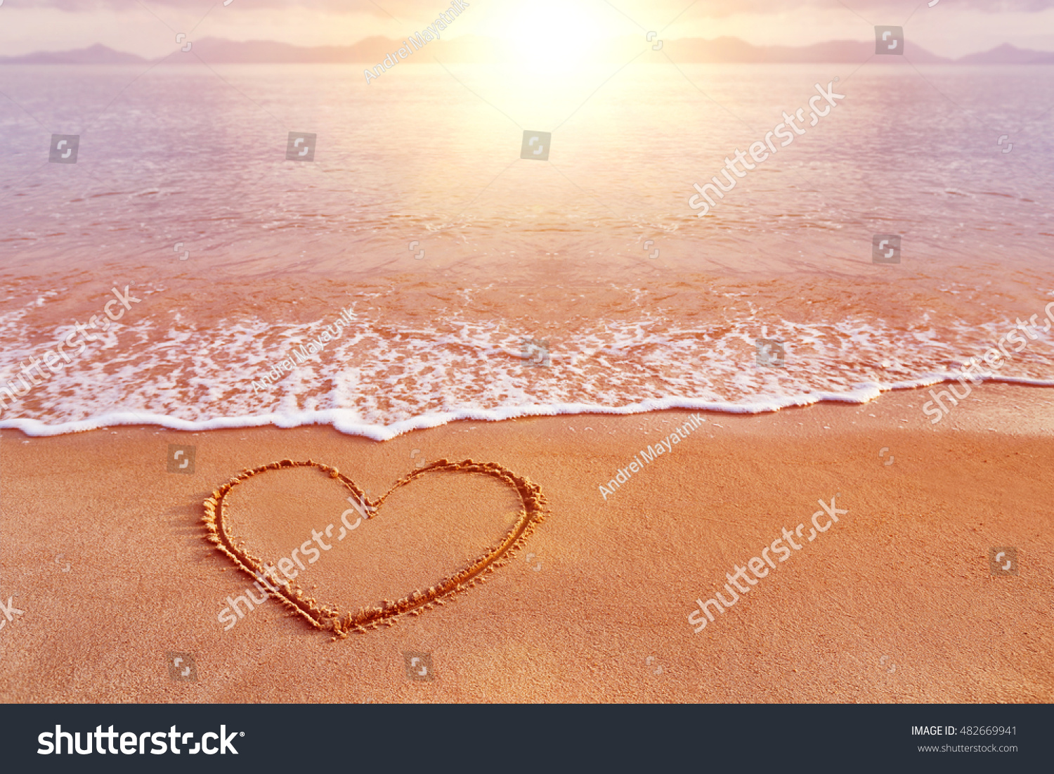 Amazing sea sunrise view with a hand drawn heart as a symbol of love at golden sand.