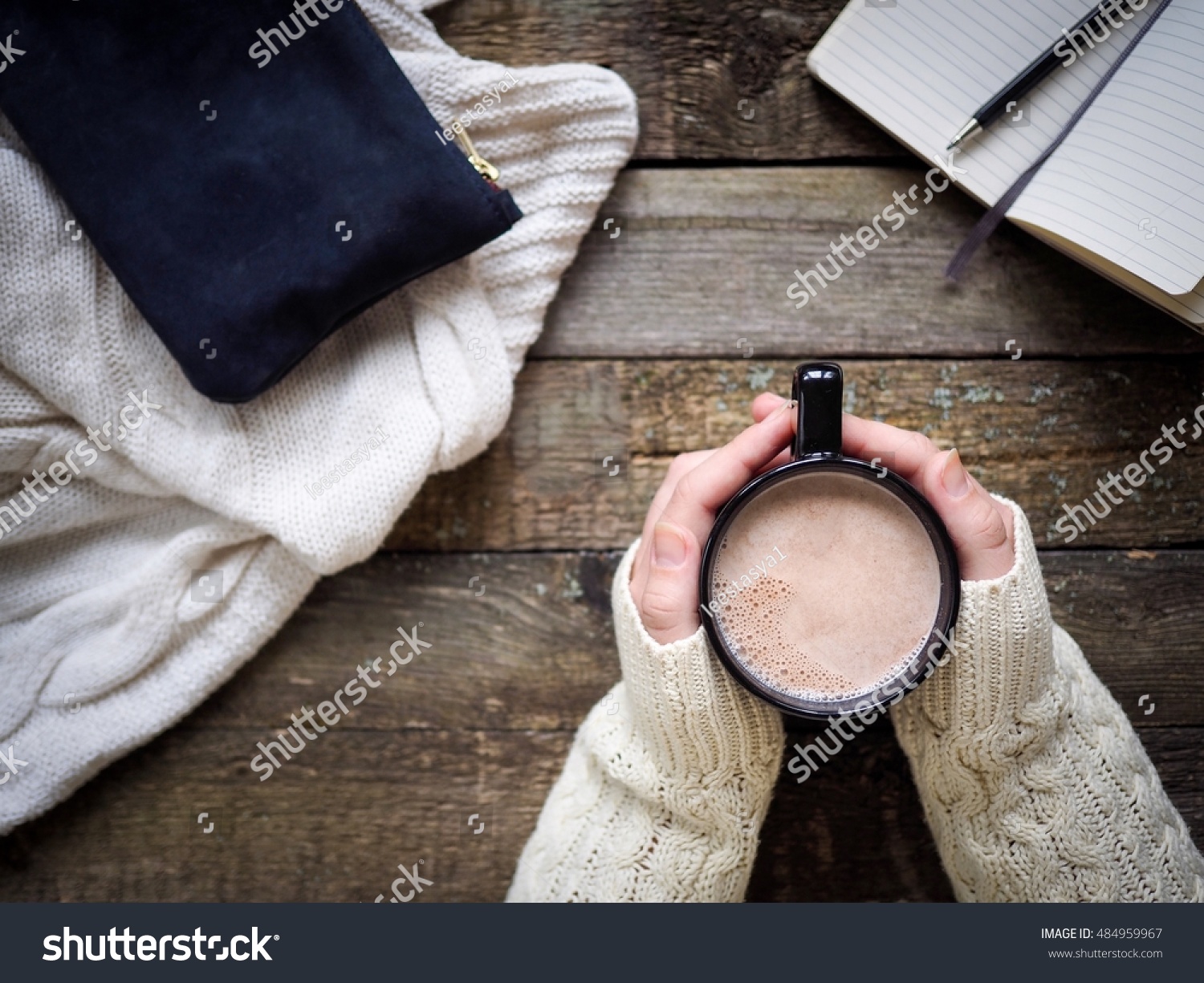 Cup of cocoa in hands and office  staff on wooden table