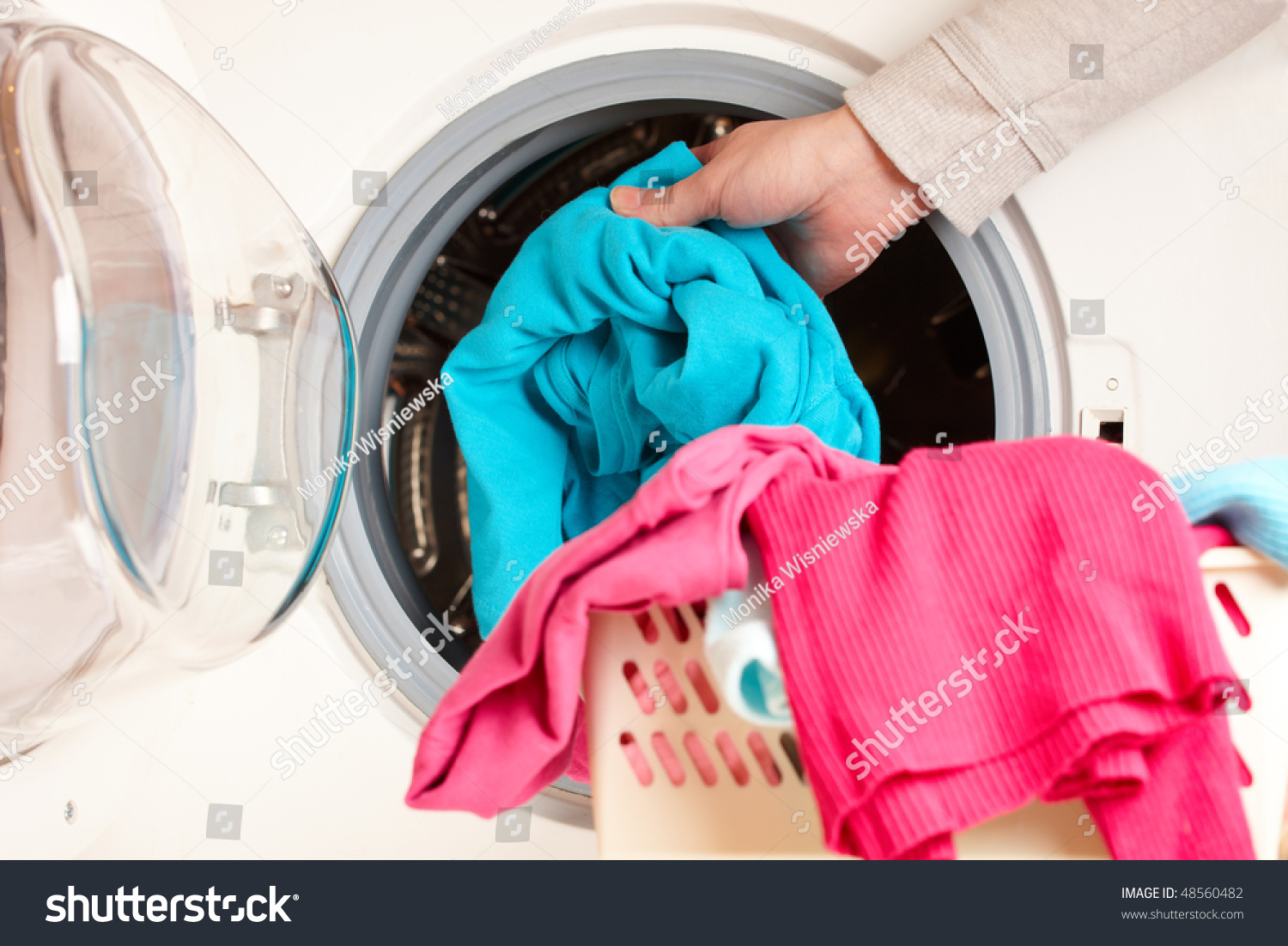 Close-up on female hand putting colorful clothes into washing machine drum