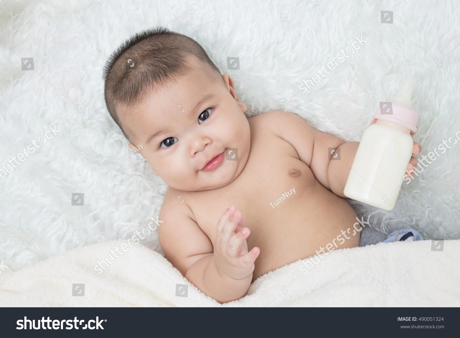 Baby lying on the white carpet and drinking milk from a bottle.