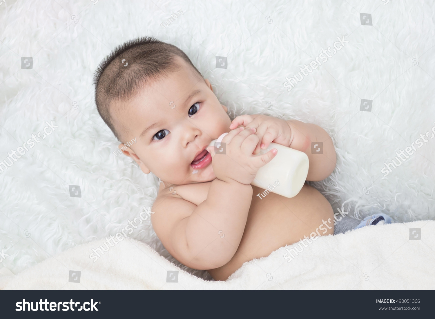 Baby lying on the white carpet and drinking milk from a bottle.