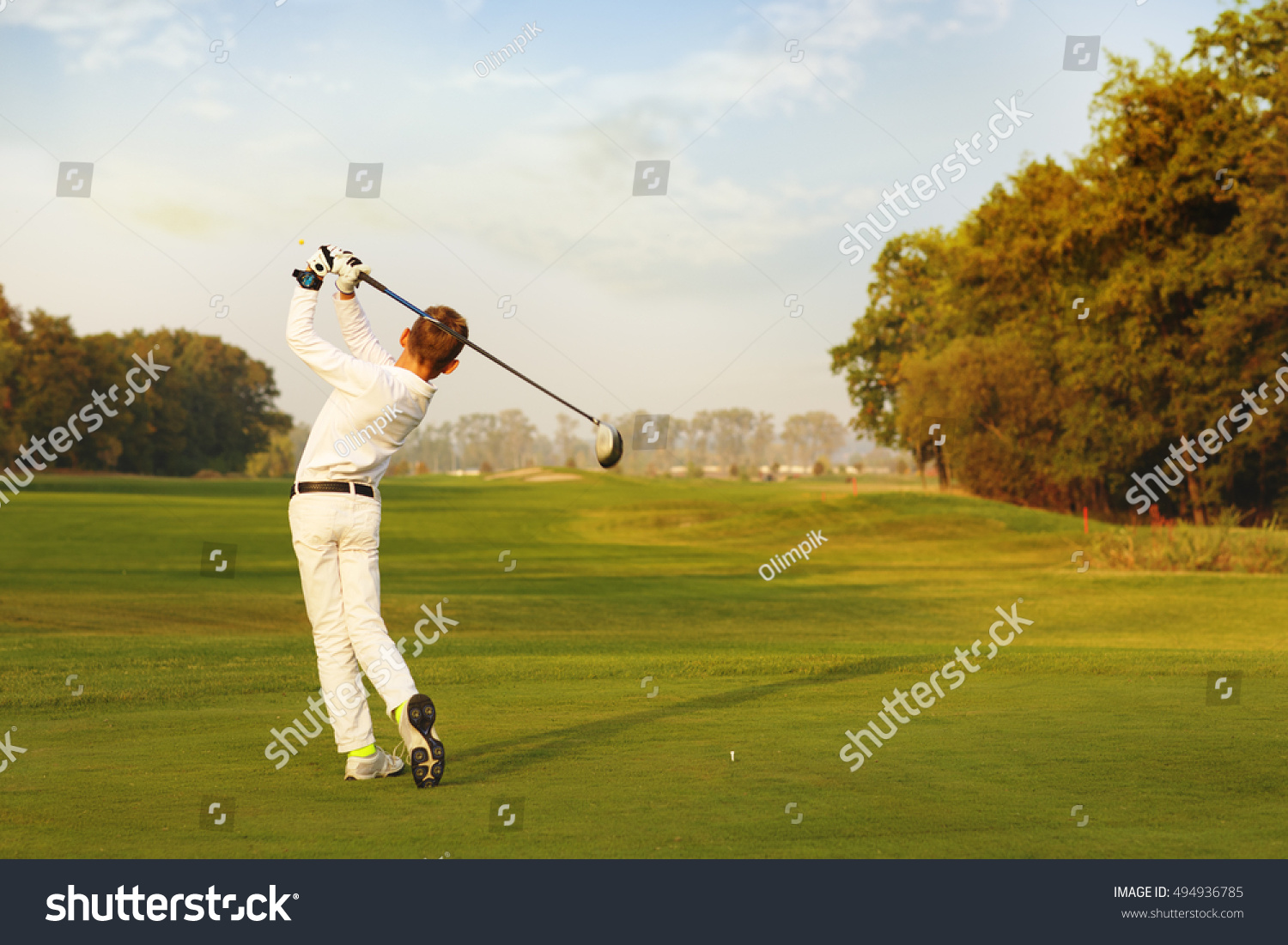 Boy golf player hitting by iron from fairway at autumn evening