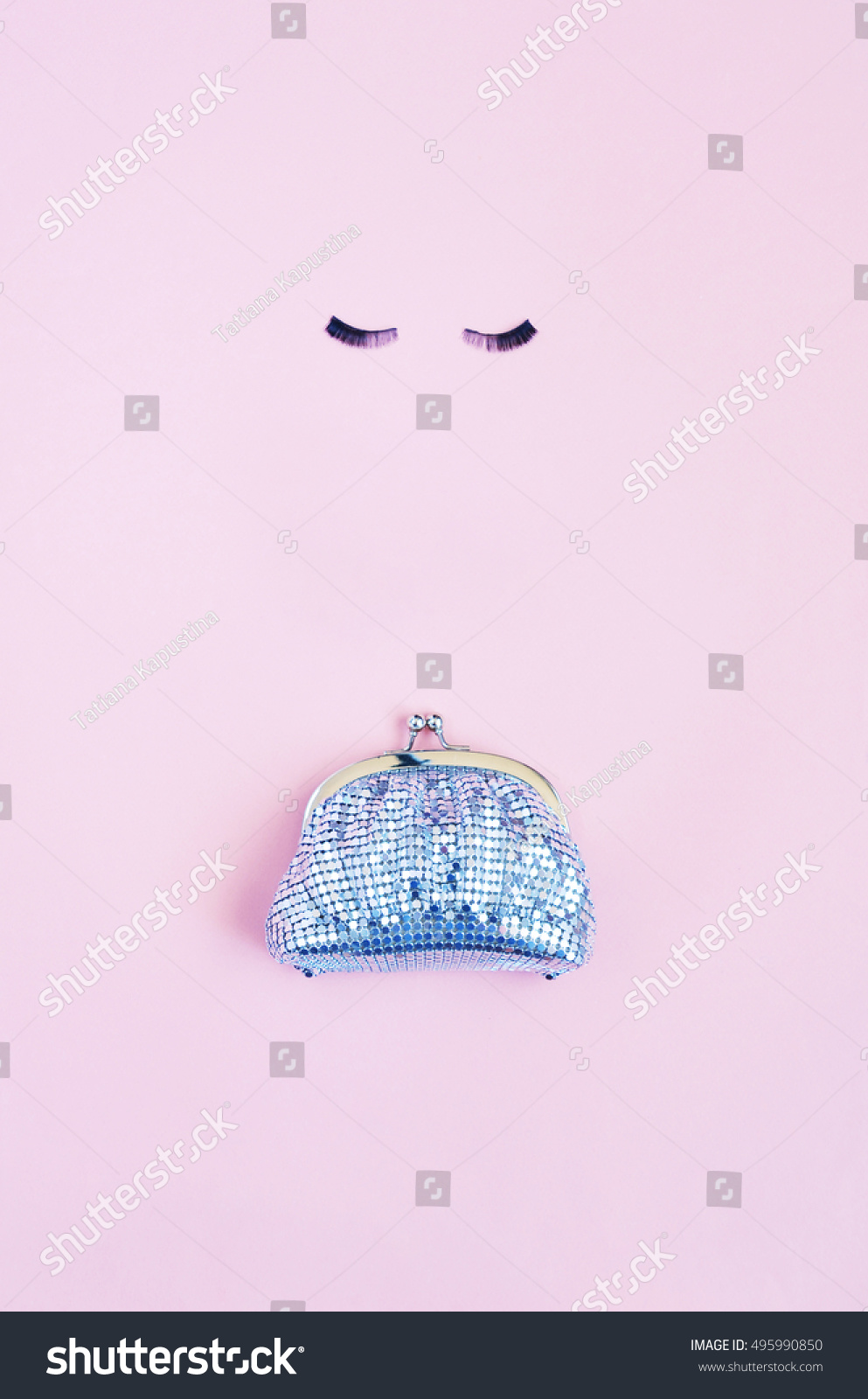 A shiny silver female purse and eyelashes on light pink background