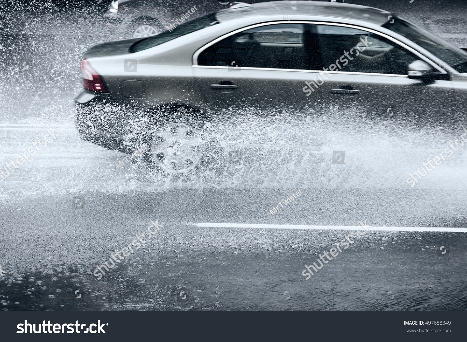flooded city road with rain puddles and with riding cars splashing water from the wheels