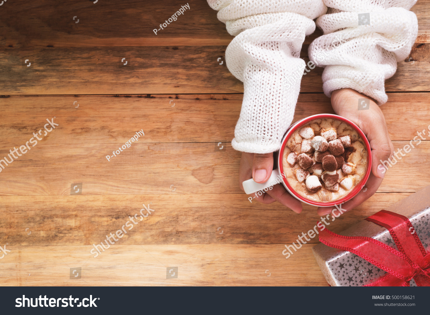 female hand holding cup of hot cocoa or chocolate with marshmallow on wooden table from above