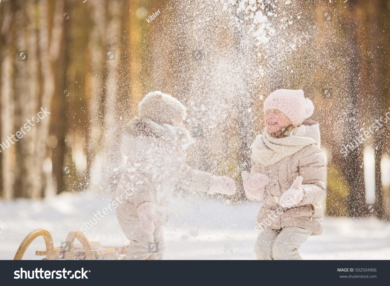 Portrait of two little girls play with snow in a park in winter