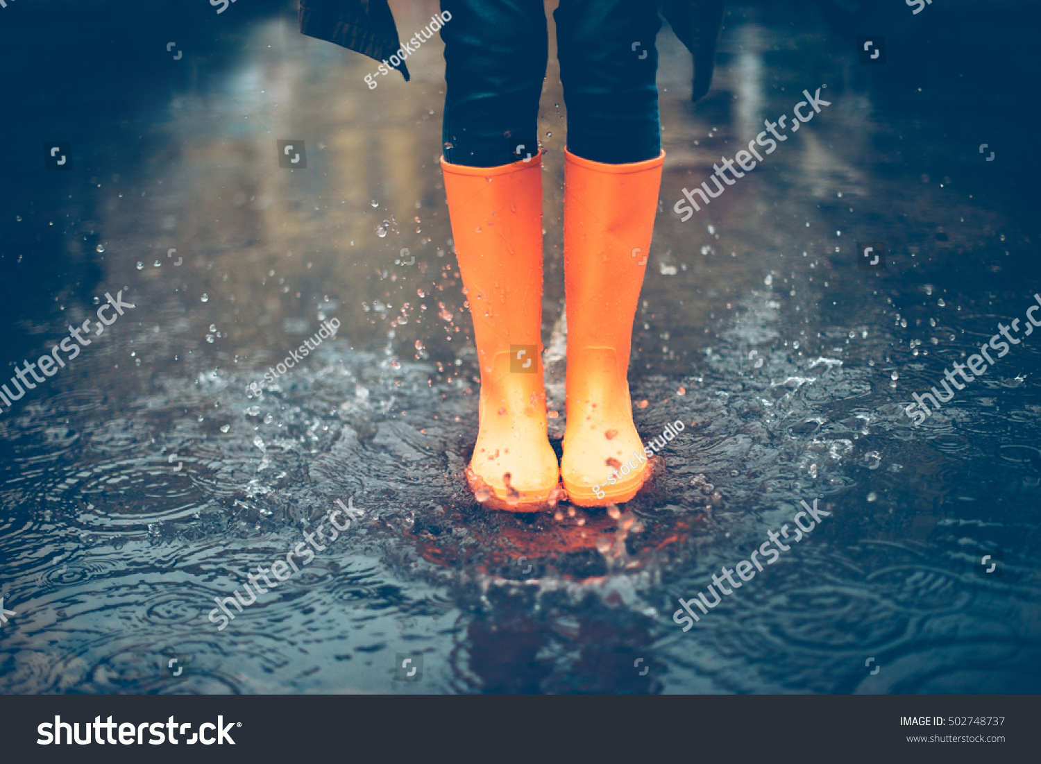 Feeling protected in her boots. Close-up of woman in orange rubber boots jumping on the puddle