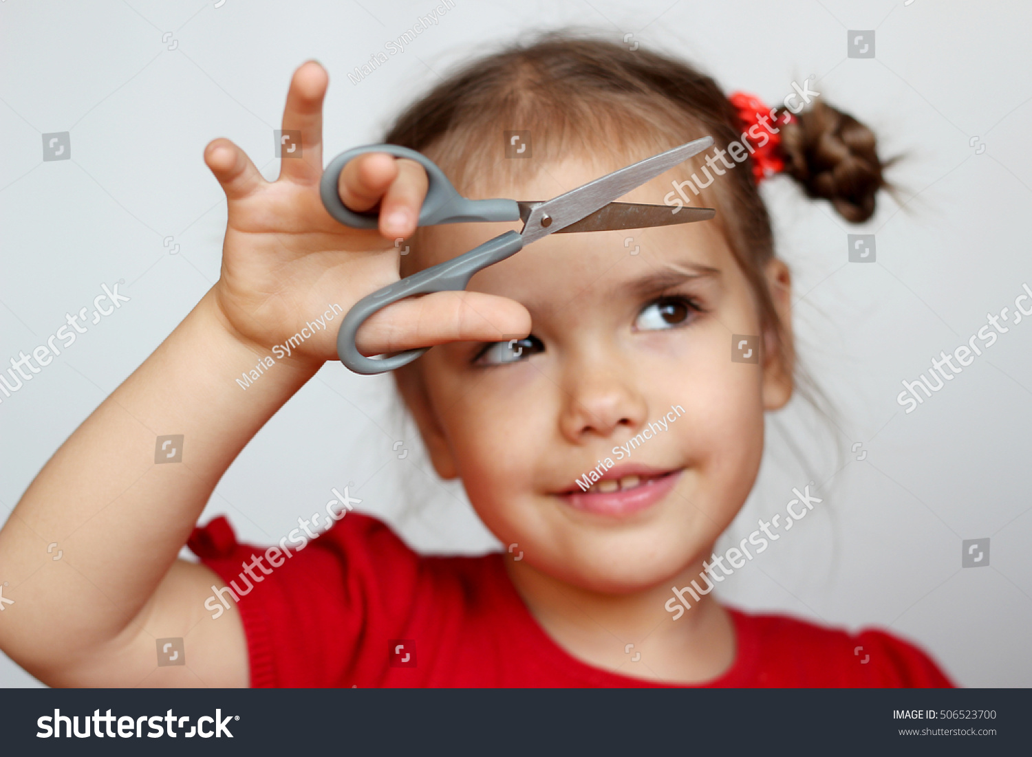 Cute little girl cutting hair to herself with scissors funny look