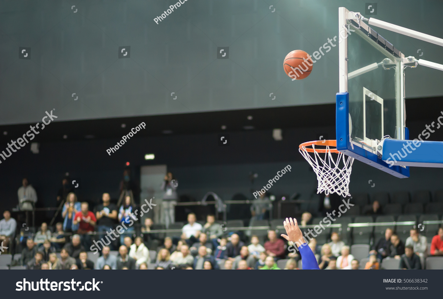 Basketball Hoop and ball are on a background of fans sitting in the stands. Basketball ball flies into the ring