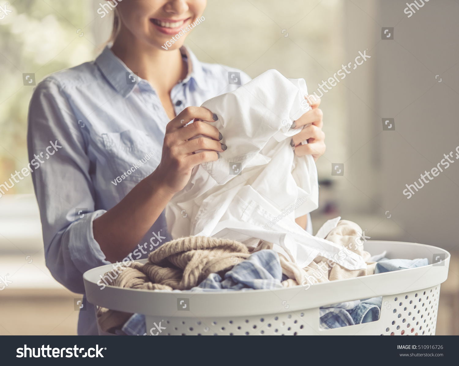 Cropped image of beautiful young woman is smiling while doing laundry at home