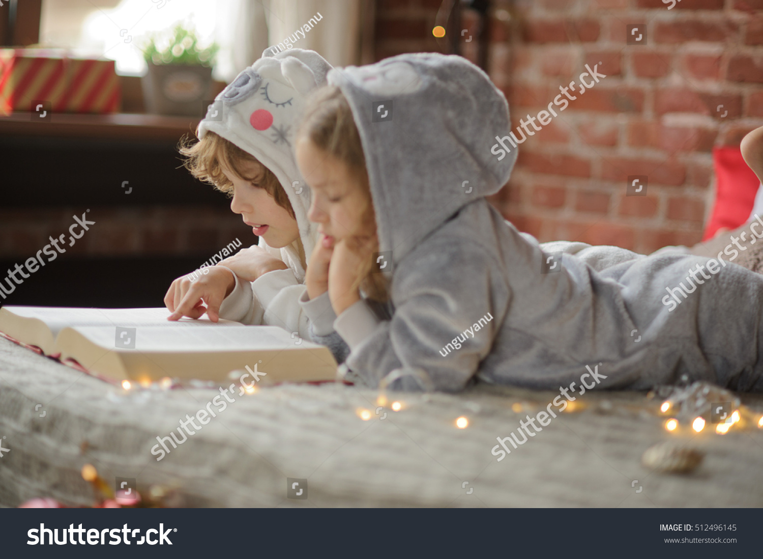 Christmas Holidays. Two children brother and sister lie on big bed and read Christmas tales. Children dressed in fluffy pajamas like little cute animals. Before them the huge book. Magic Christmas.