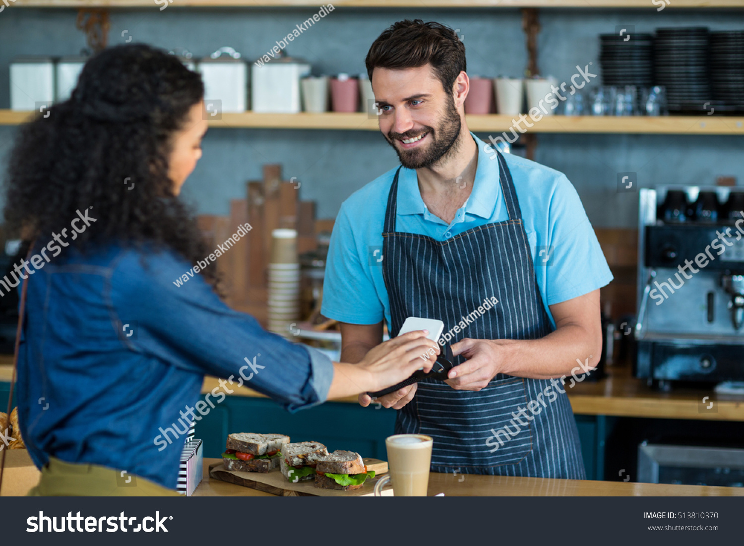 Woman paying bill through smartphone using NFC technology in cafe