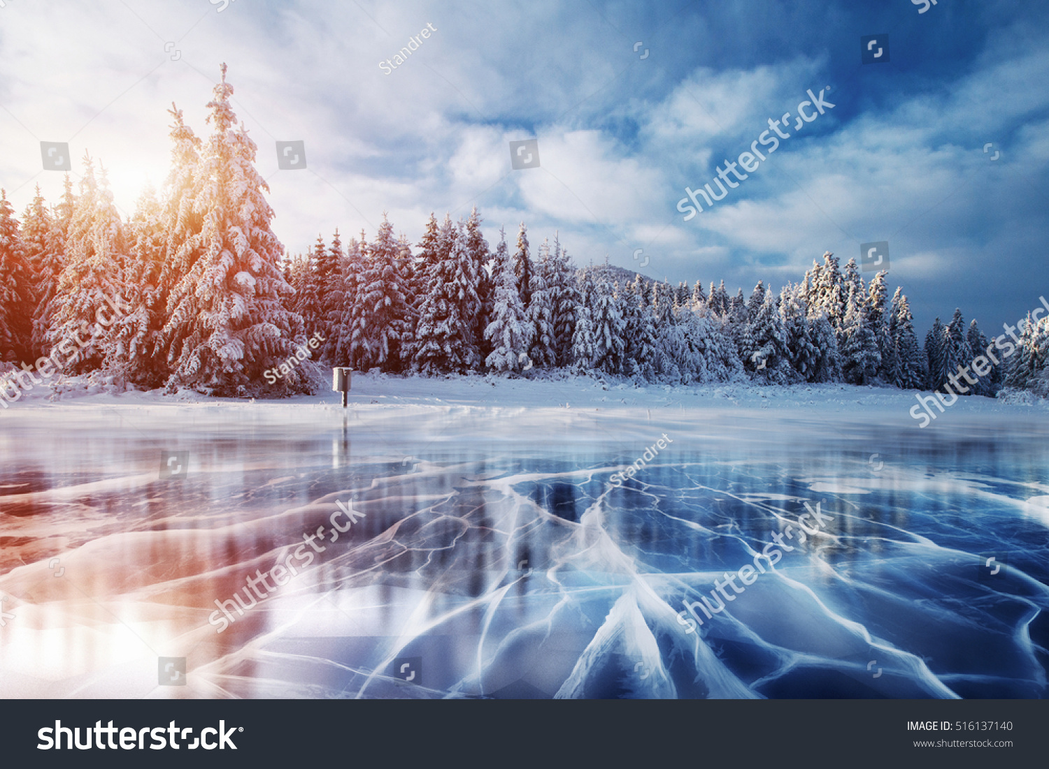 Cracks on the surface of the blue ice. Frozen lake in winter mountains. It is snowing. The hills of pines. Carpathian Ukraine Europe.