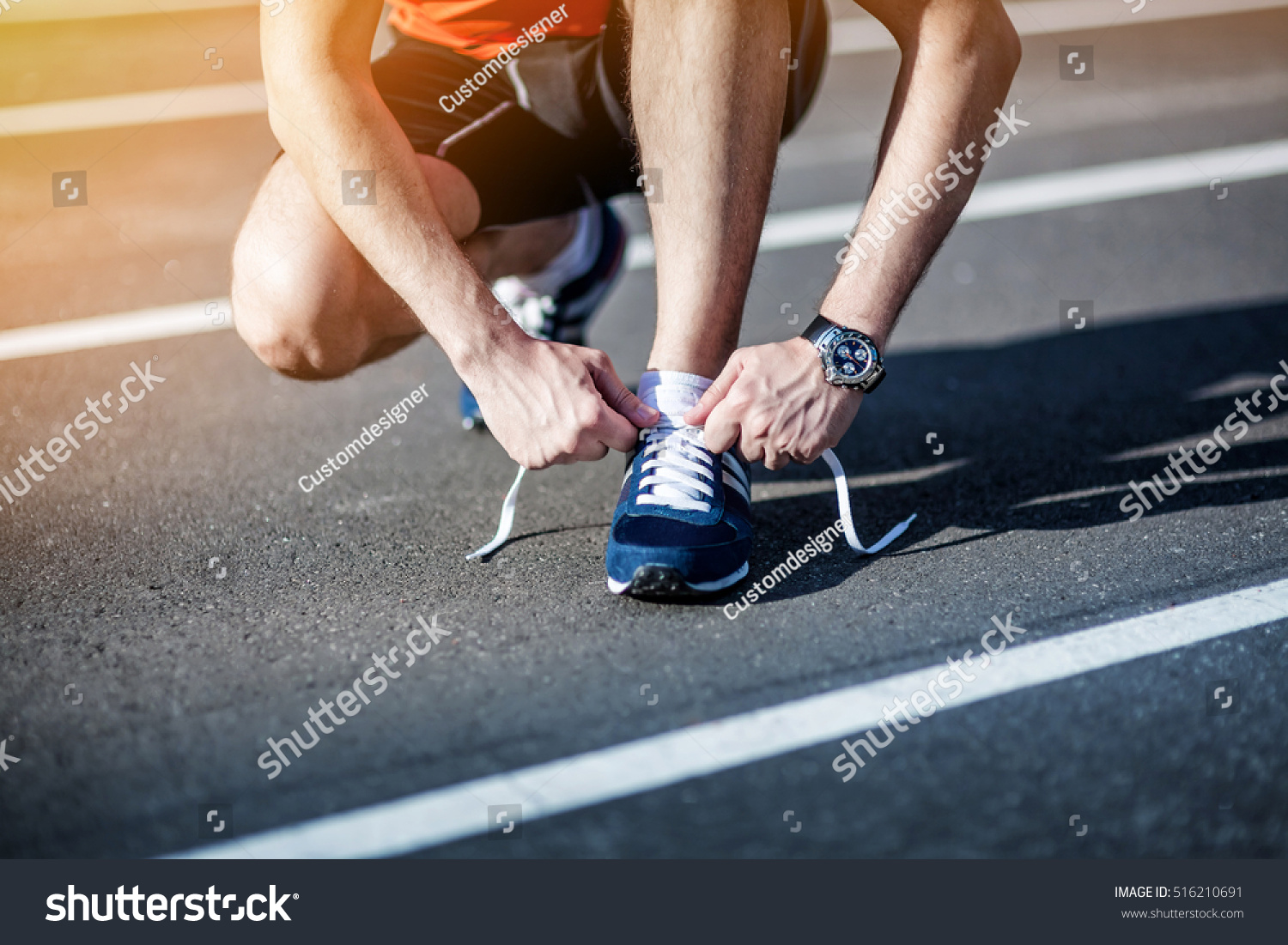Young Man Runner tying his shoes on a running track. Shoelaces Urban