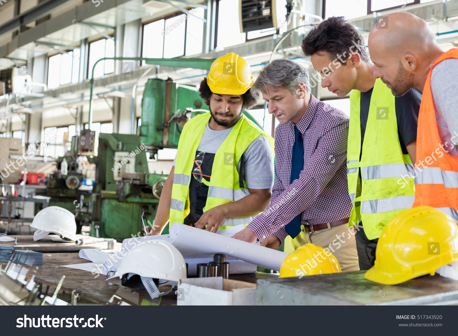 Male supervisor with workers discussing over blueprints in industry