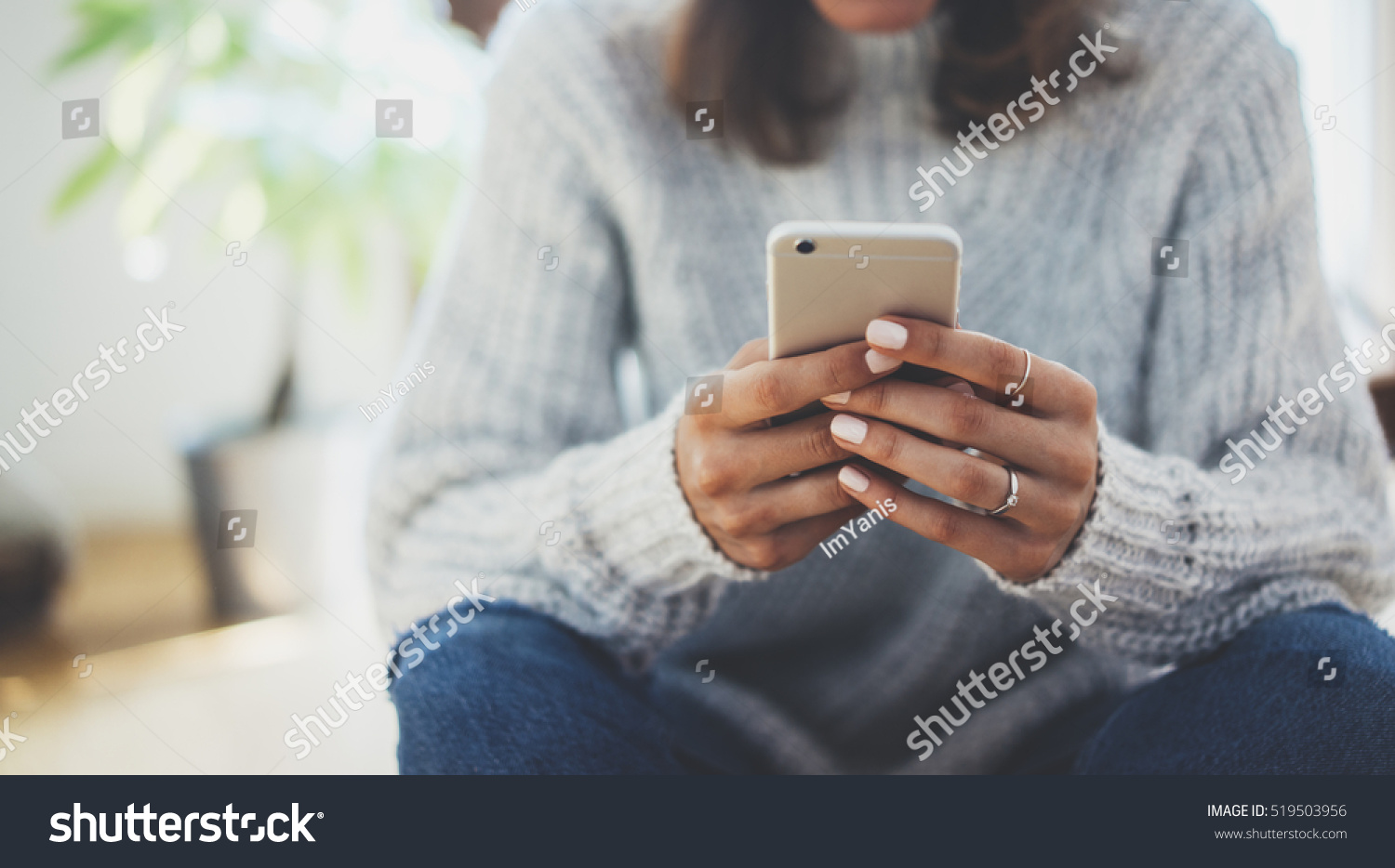 Close-up image of young hipster girl sitting at cozy home interior and using modern smartphone device female hands typing text message via cellphone social networking concept