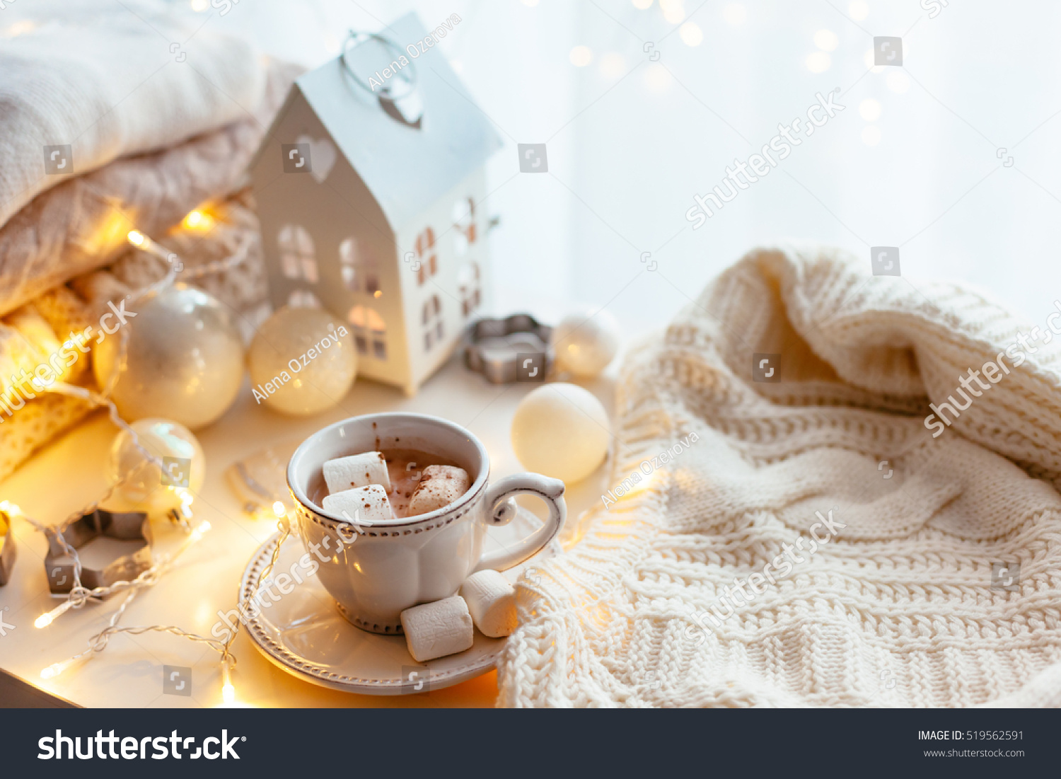 White Christmas decor: warm sweater cup of hot cocoa with marshmallow and led string lights. Winter mood holiday decoration.