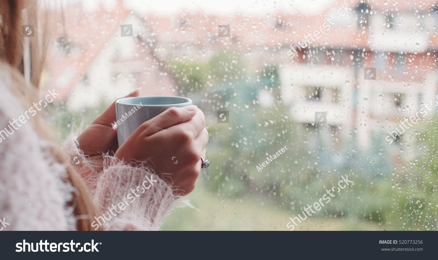 Young Woman Enjoying her morning coffee or tea Looking Out the Rainy Window. Beautiful romantic unrecognizable girl drinking hot beverage at cozy home. Rainy Day Mood.