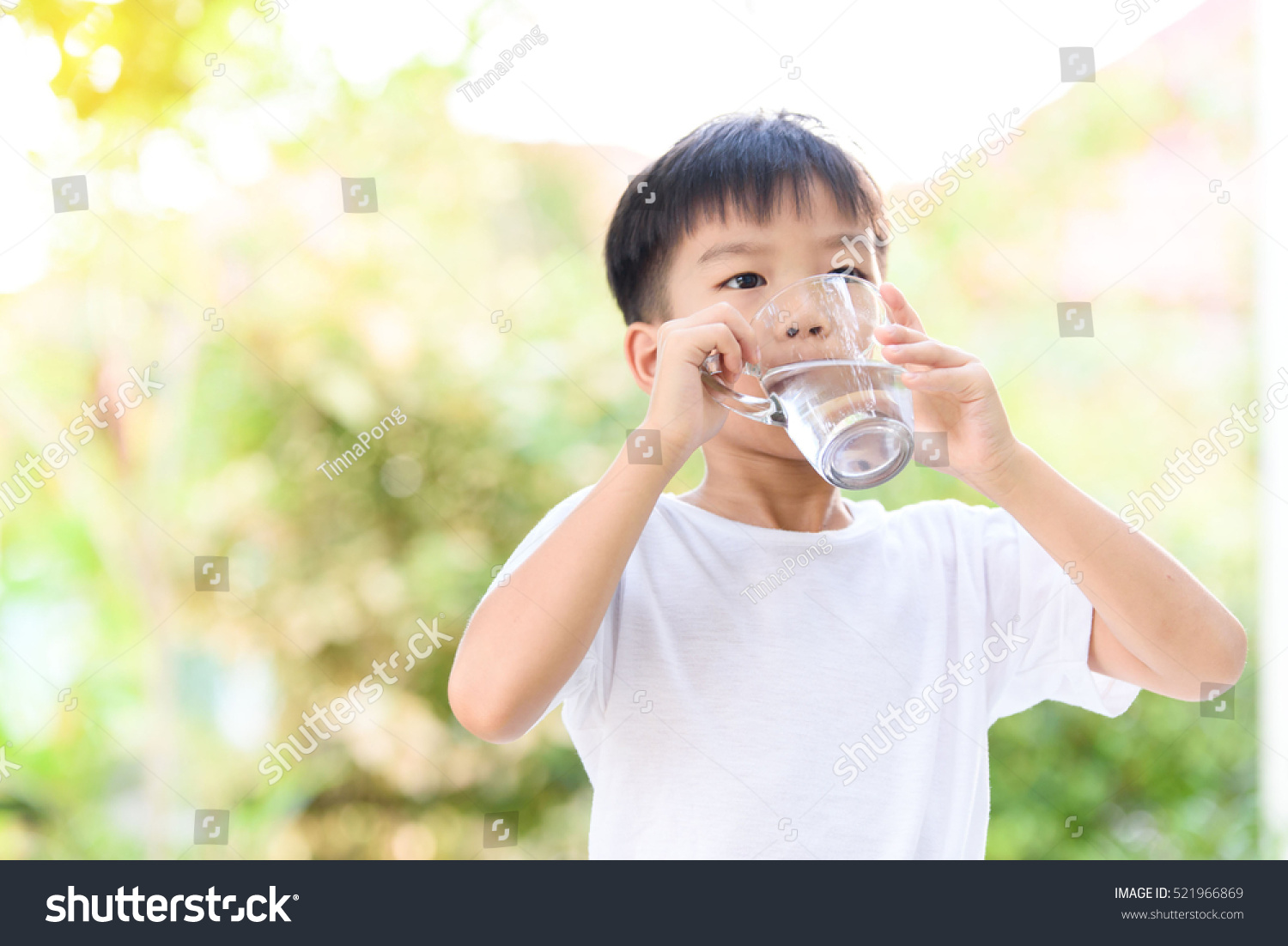 Young Thai boy drinking water from glass in the garden