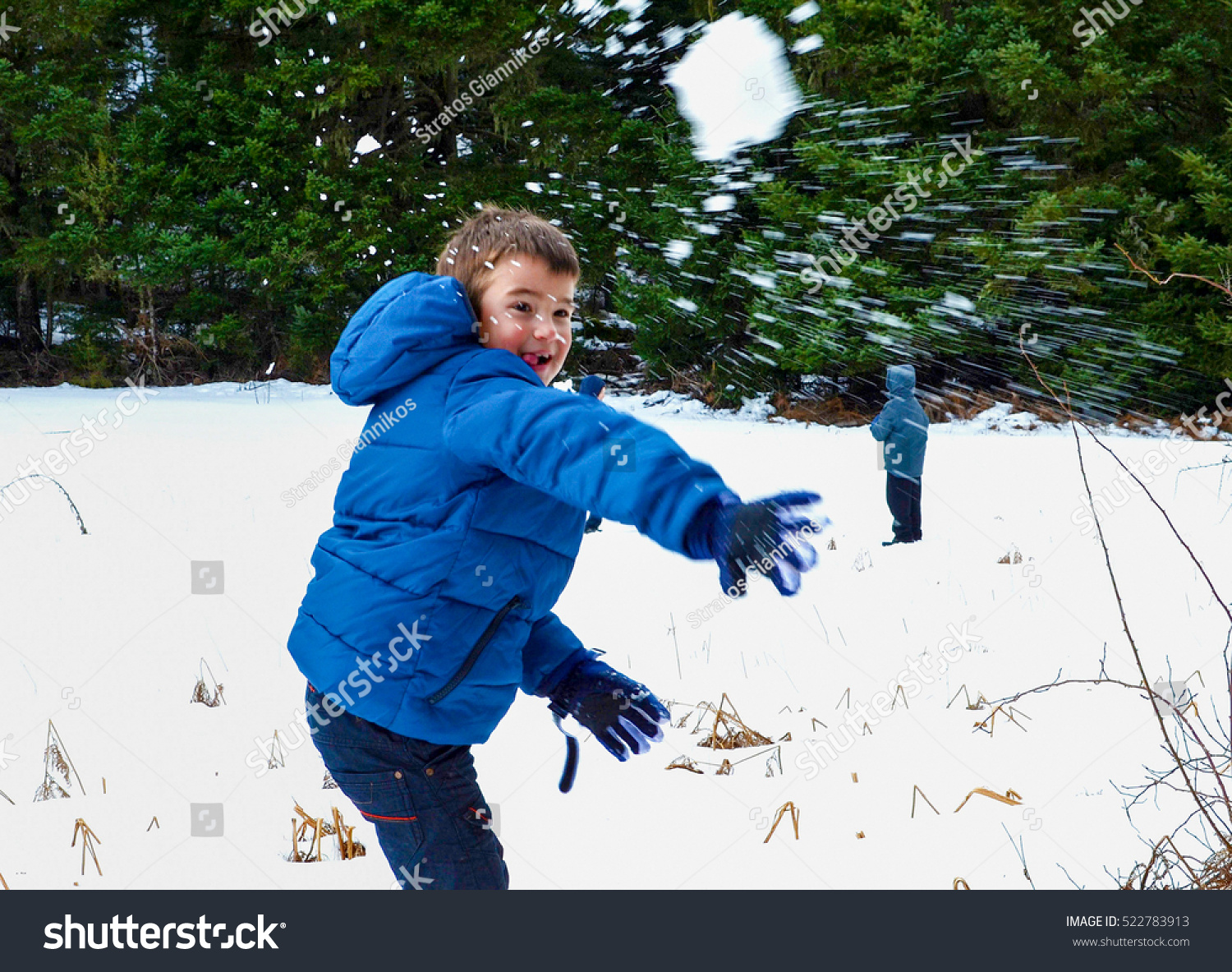 Boy in blue warm coat having fun in beautiful winter place with snowballs
