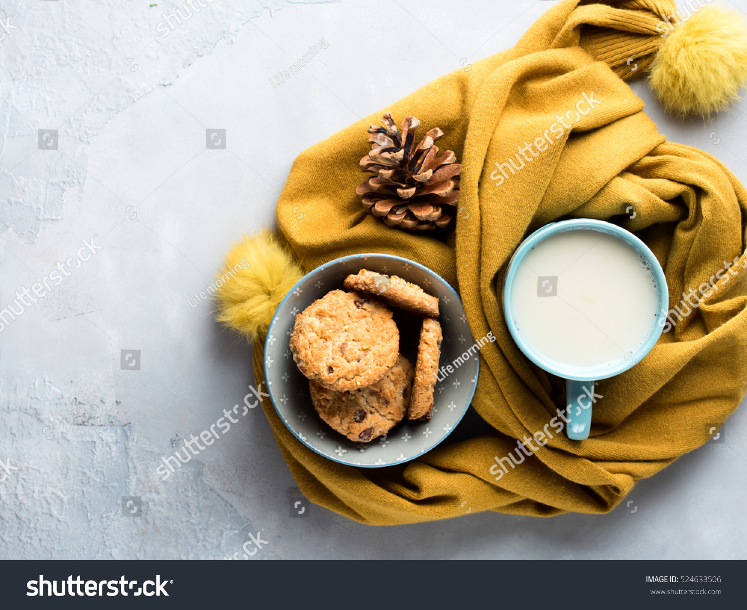 Mug of tea with milk and cookies with chocolate chips in a soft yellow winter scarf on gray background. Coffee break for home relax. Top view