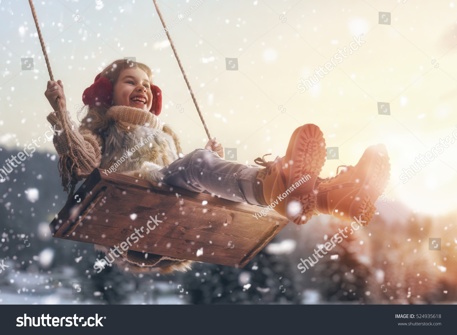 Happy child girl on swing in sunset winter. Little kid playing on a winter walk in nature.