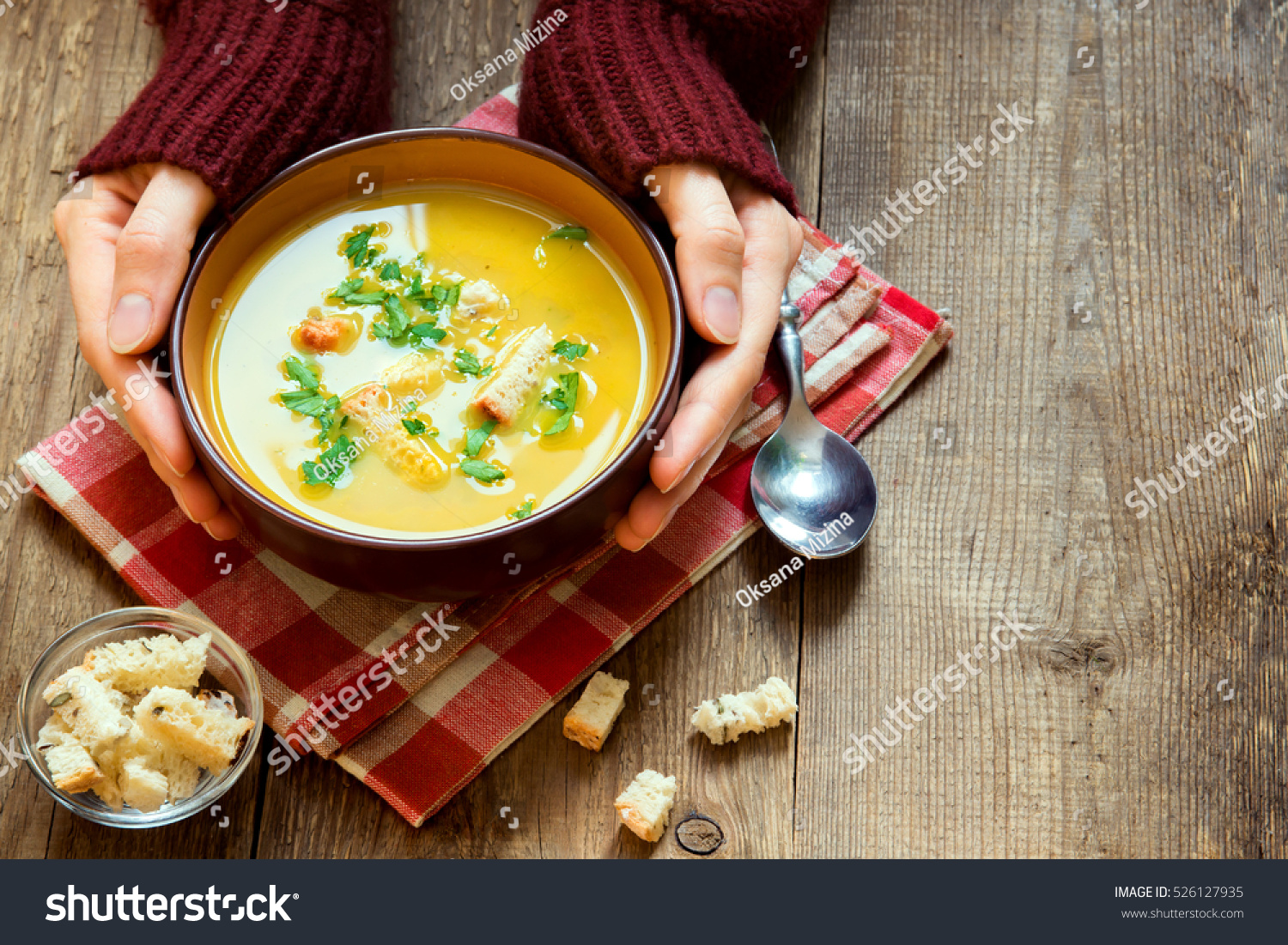 Woman hands holding bowl of vegetable soup with parsley and croutons over wooden background - healthy winter vegetarian food