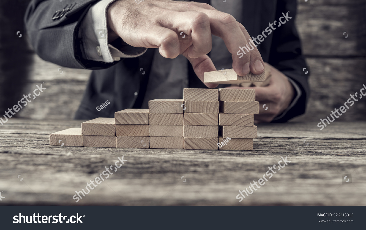 Businessman building a graph or ladder of success on old rustic wooden table.