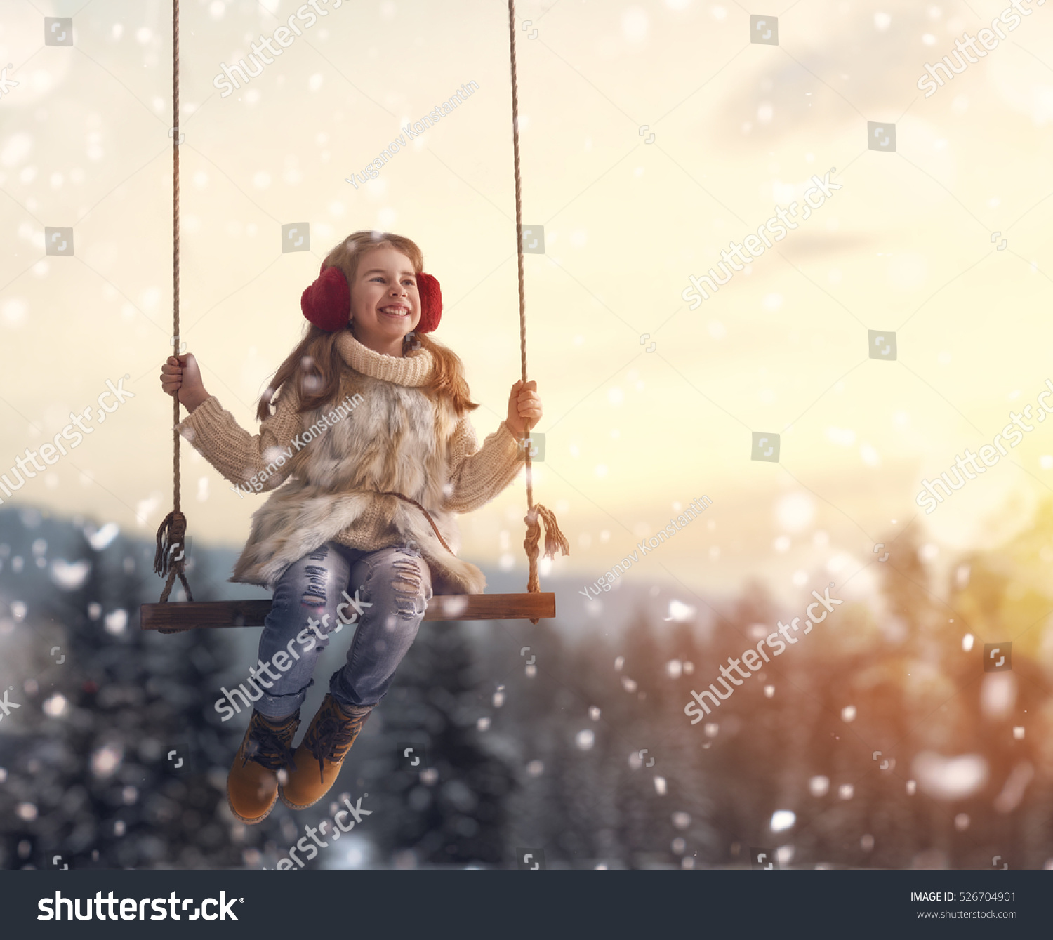 Happy child girl on swing in sunset winter. Little kid playing on a winter walk in nature.