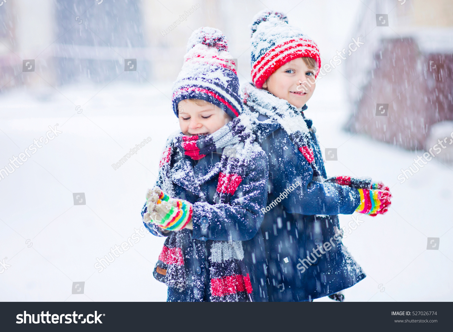 Two little kid boys in colorful clothes playing outdoors during snowfall. Active leisure with children in winter on cold days. Happy siblings and twins having fun with snow