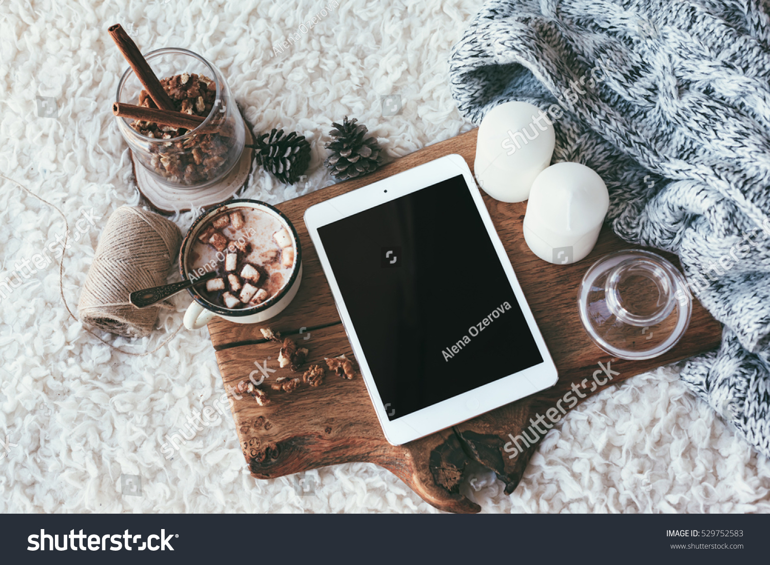Winter homely scene scandinavian style. Warm knit sweater tablet pc with blank screen candles cup of sweet cocoa with marshmallows and other decor on wooden tray in bed. Lazy cold weekend.