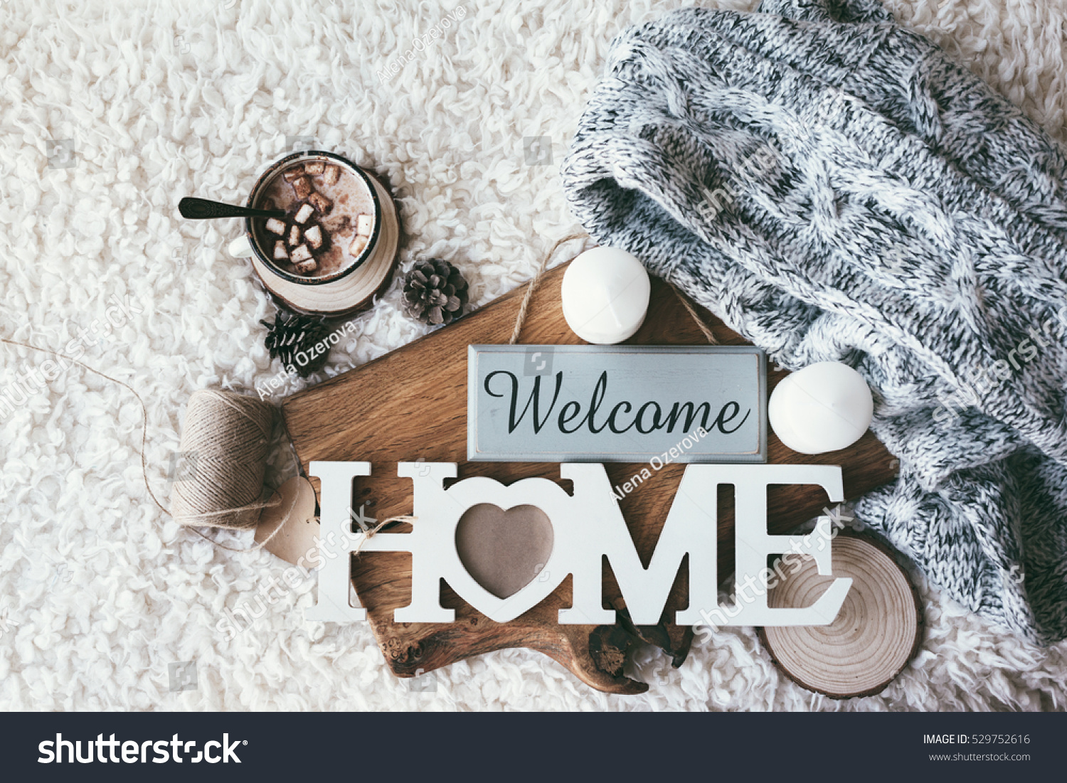Winter homely scene scandinavian style. Warm knit sweater candles cup of sweet cocoa with marshmallows and other decor on tray in bed. Wooden craft letters Welcome Home. Lazy cold weekend.