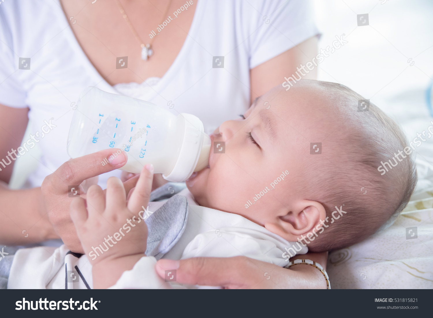 Asian mother holding and feeding milk for her child from plastic bottle at home