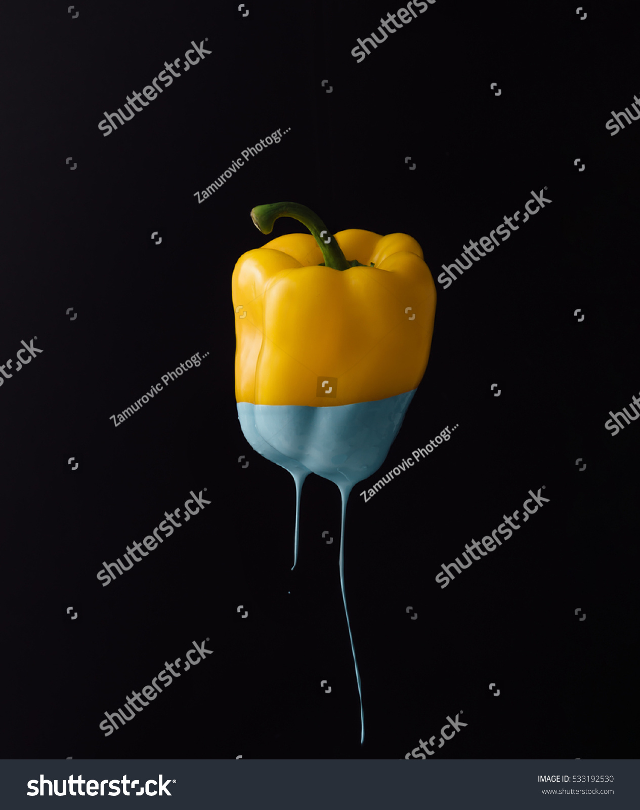 Yellow bell pepper with dripping blue paint on dark background. Minimal food concept.