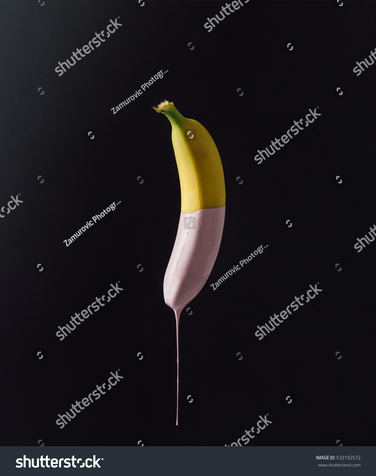 Banana with dripping pink paint on dark background. Minimal food concept.