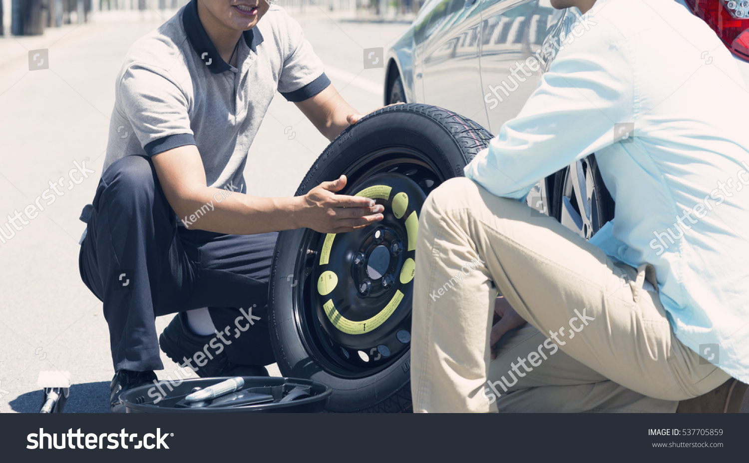 Picture of a male mechanic replacing a car tire with his client on the road