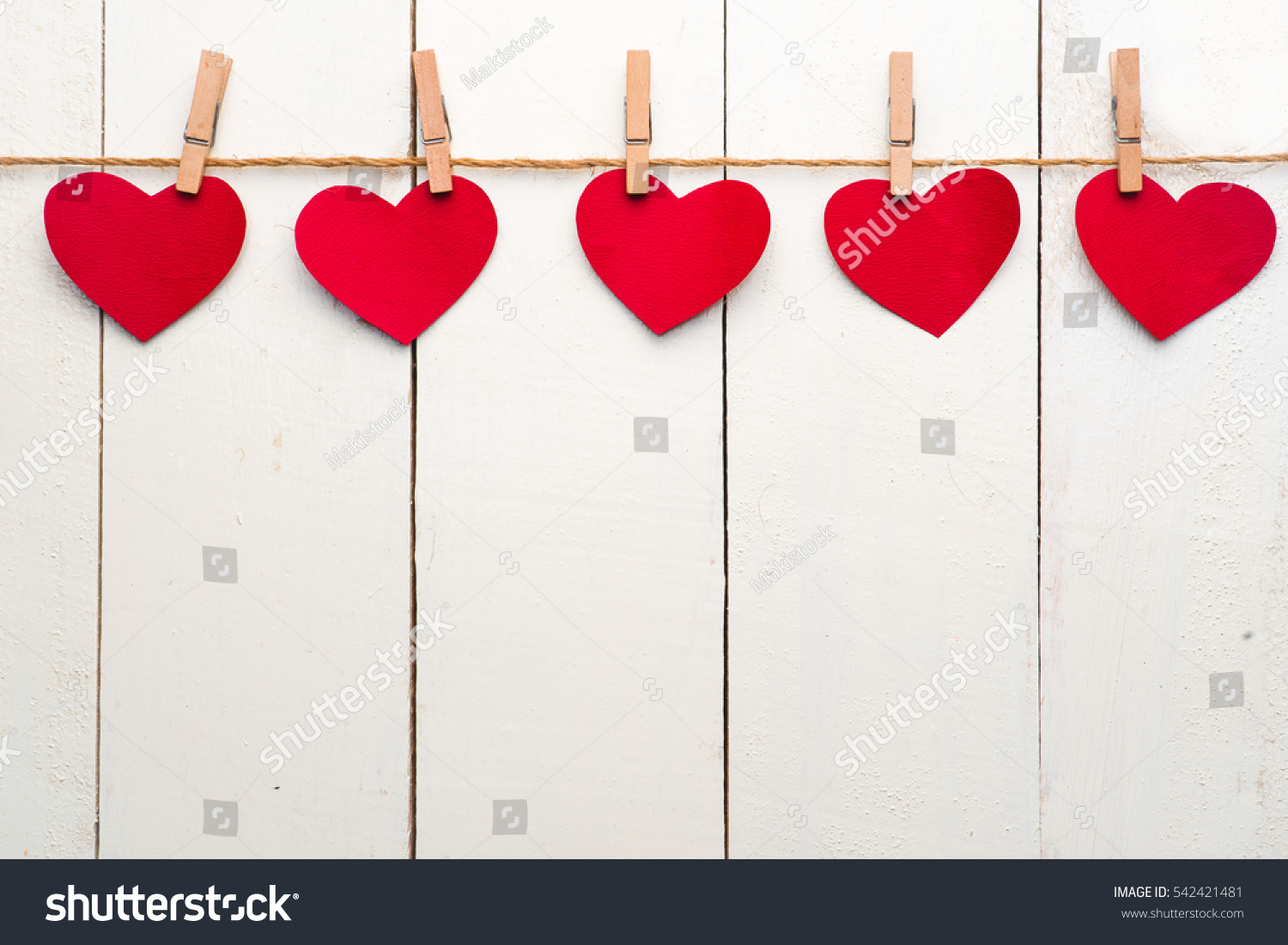 Colorful heart hanging on the clothesline on white wooden background.