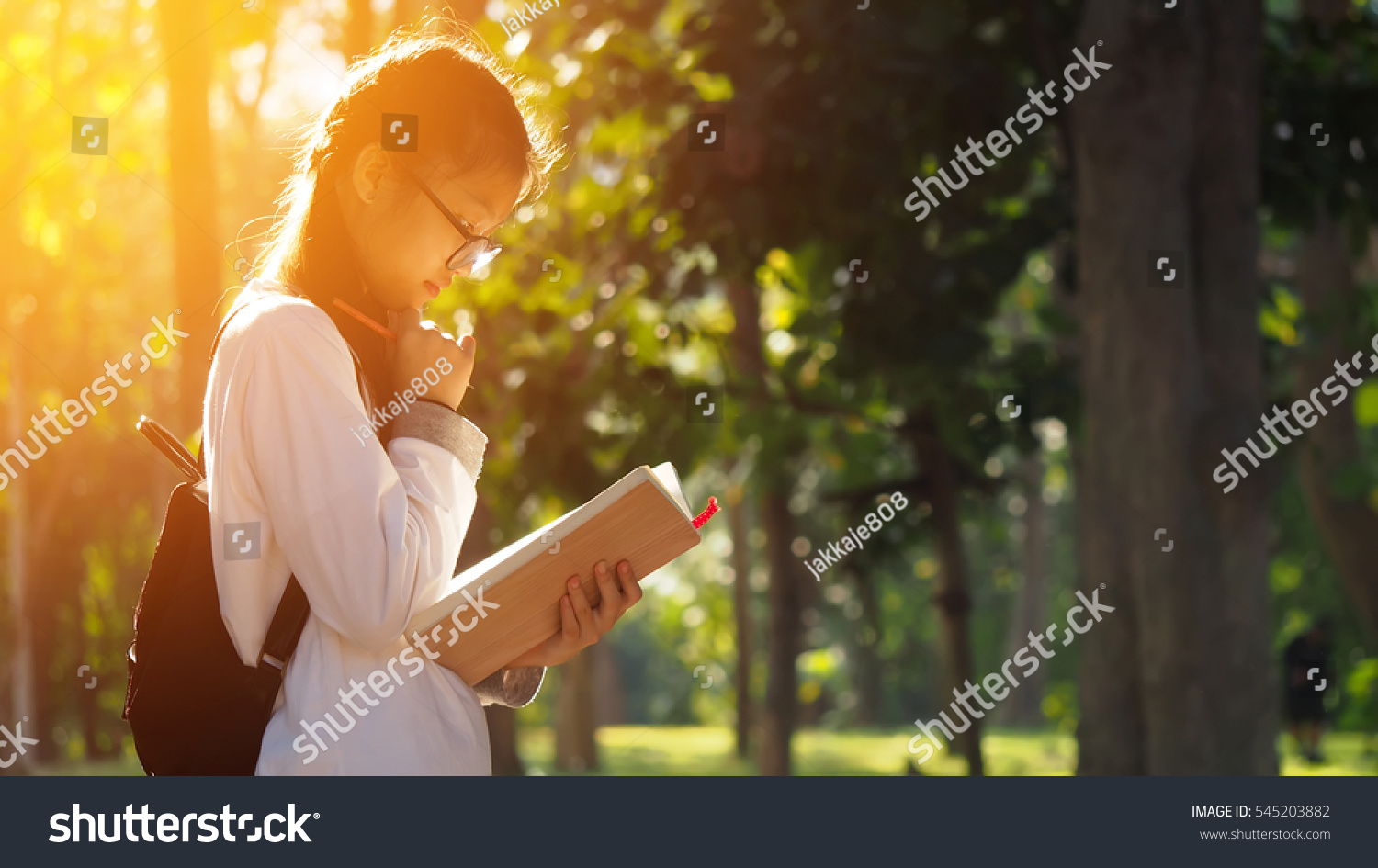 Asian student girl reading book in the park with sun shining  education background