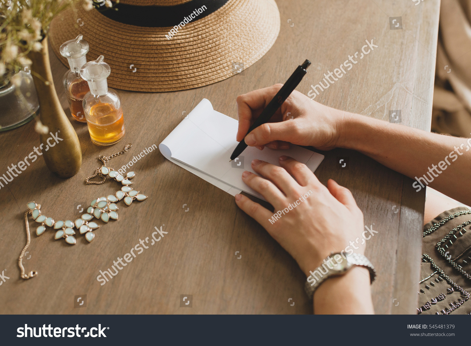 young stylish beautiful woman sitting at table in resort hotel room writing a letter holding pen straw hat vintage style hands close-up details accessories travel diary