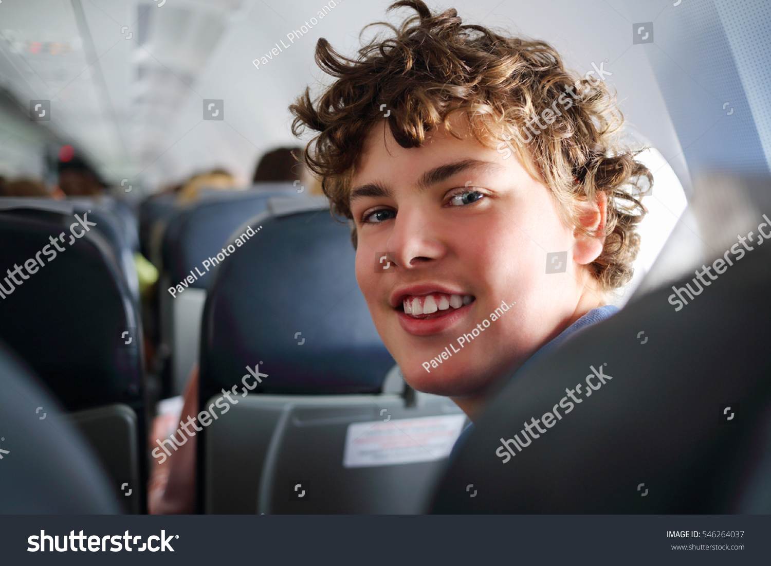 Handsome teenager boy with curly hair smiles in airplane during trip