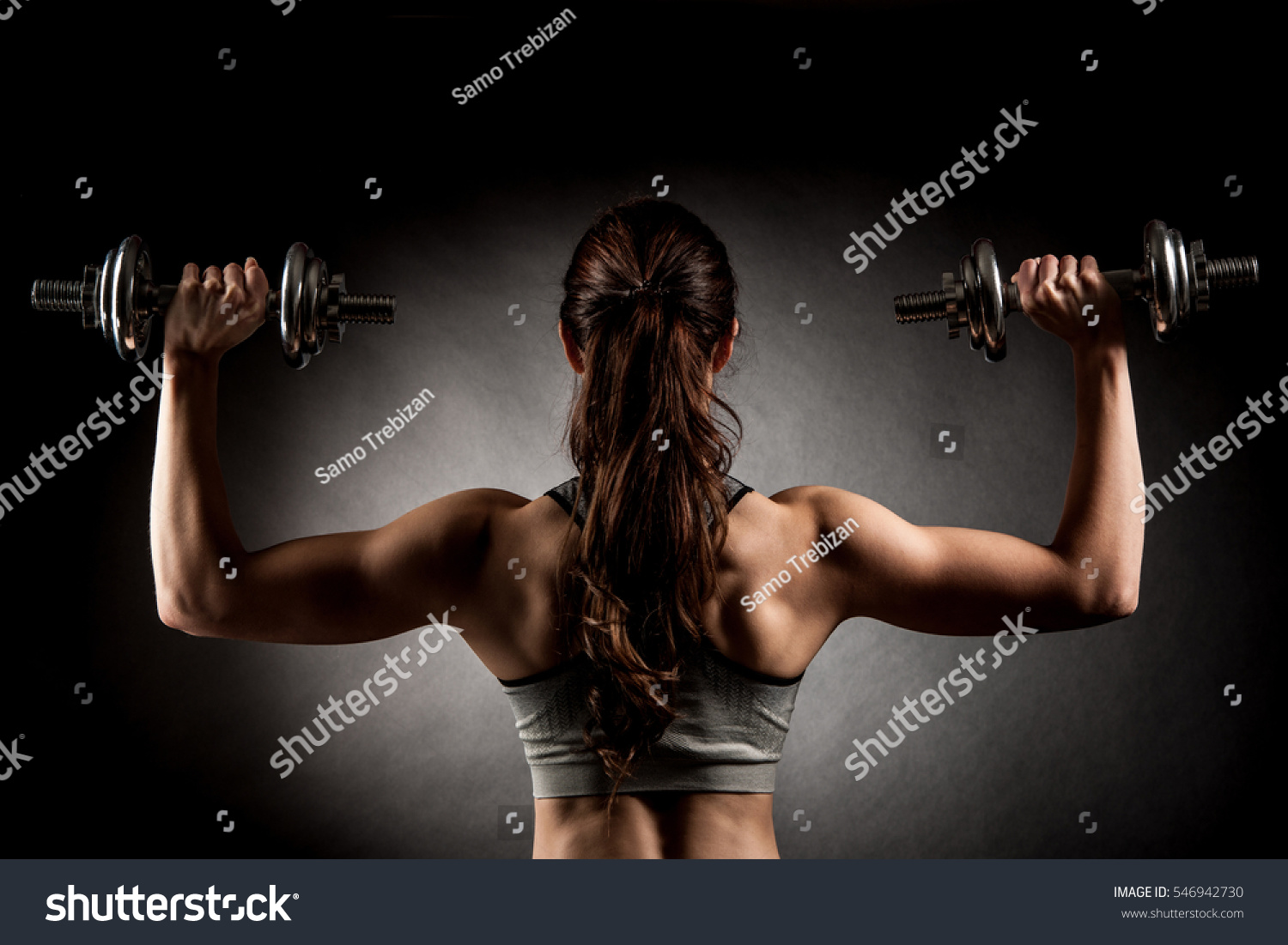 Attractive fit woman works out with dumbbells as a fitness conceptual over dark background.