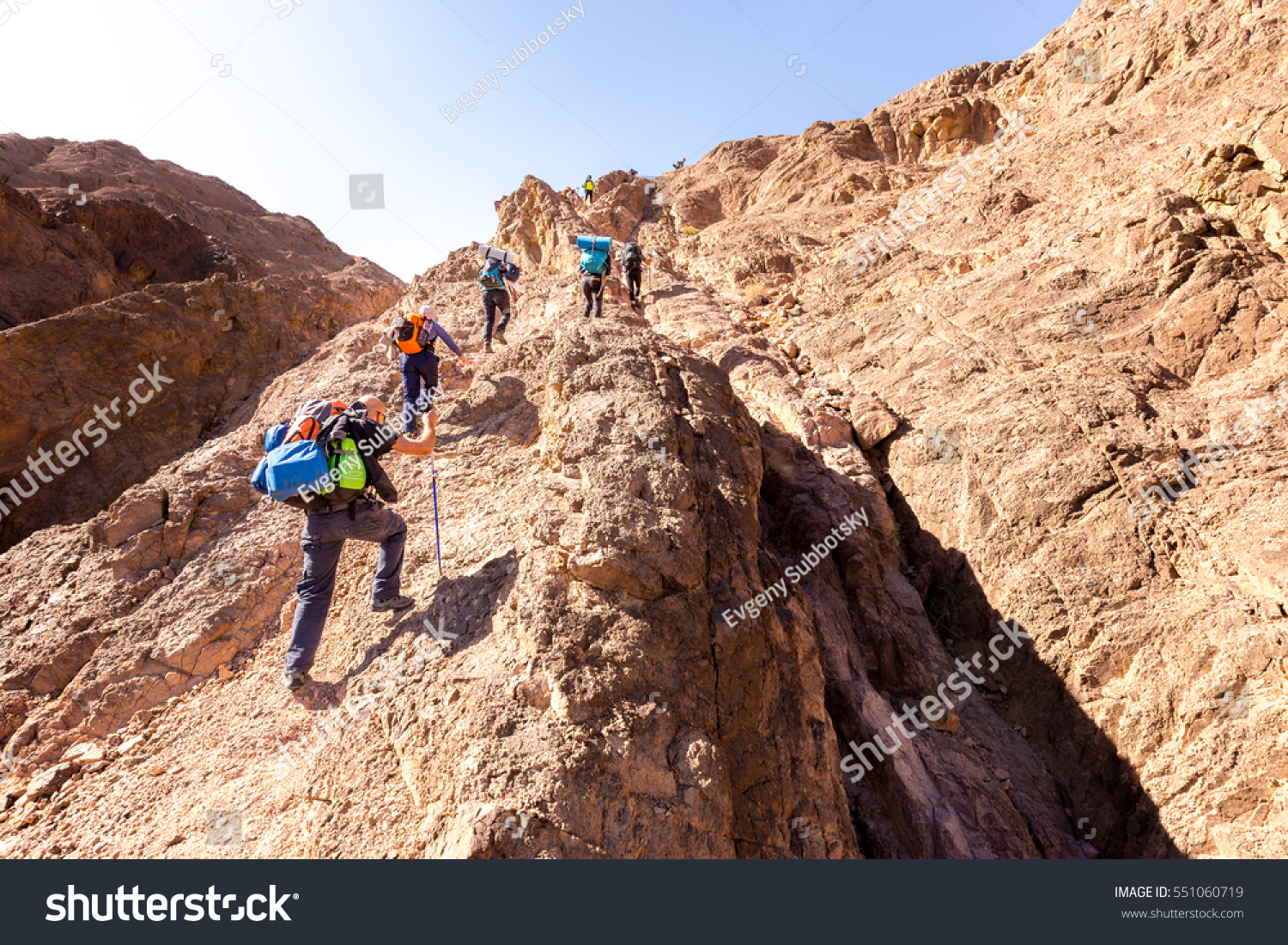 Group people backpackers tourists climbing struggling ascending rock cliff desert mountain ridge travel Negev nature Israel tourism destination hiking.