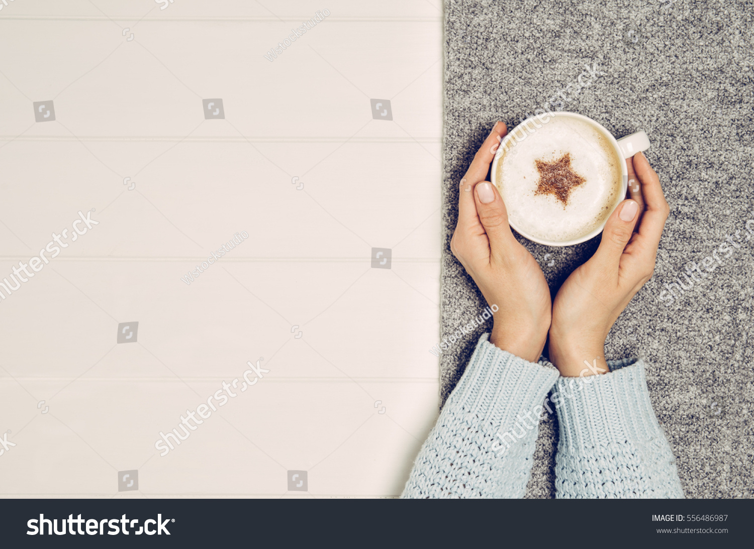Female hand holding cup of coffee on white wooden table. Photograph taken from above top view with copy space