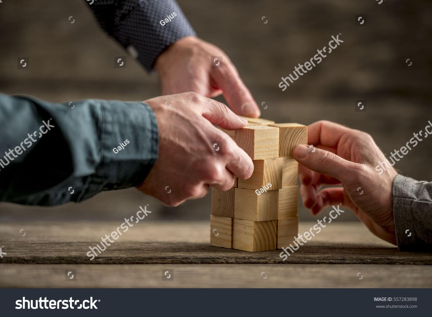 Hands of three people building a tower of wood blocks on a table  teamwork concept.