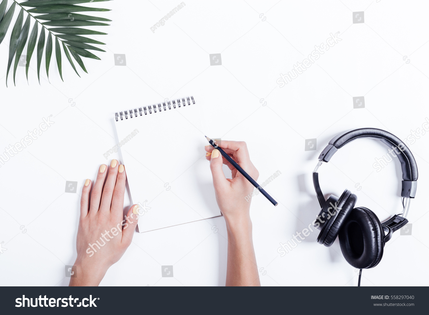 Female hands with a notebook and pencil  headphones and plant on white table  top view