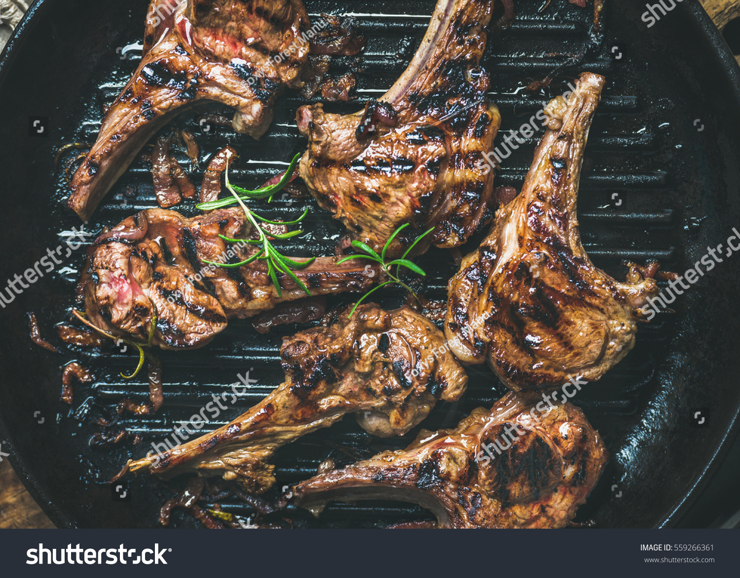 Barbecue dinner. Grilled lamb meat chops with onion and rosemary in black cast iron pan top view close-up. Slow food concept