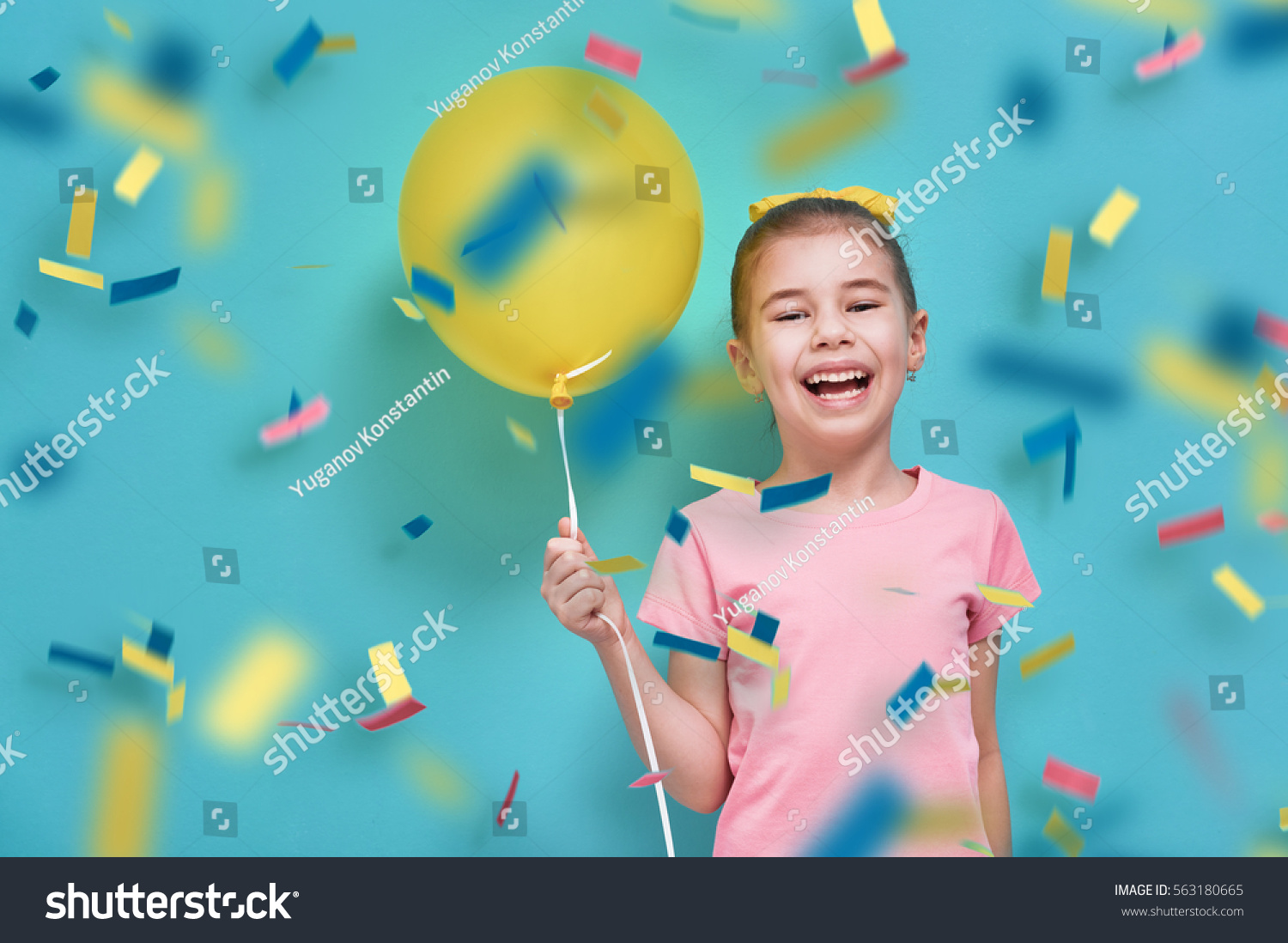 Funny child on a background of bright blue wall. Girl is having fun with balloons and confetti. Yellow  pink and turquoise colors.