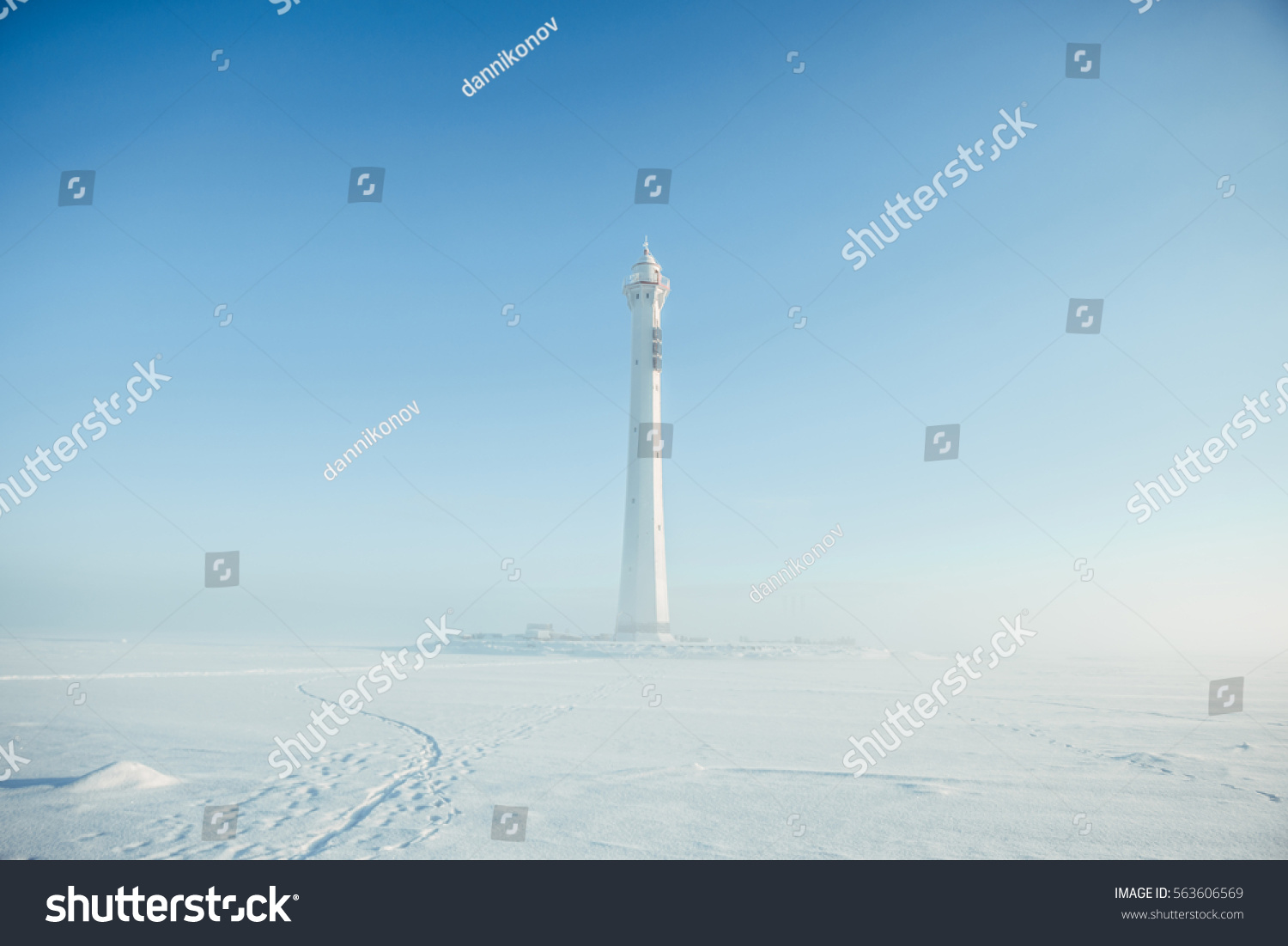 Lighthouse in a calm and desolate winter landscape. A white whitewashed lighthouse isolated over blue sky with clouds. Lighthouse on ice. Russian winter.