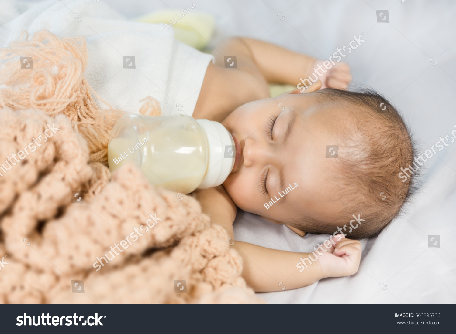 baby drinking milk from bottle and sleeping on bed at home