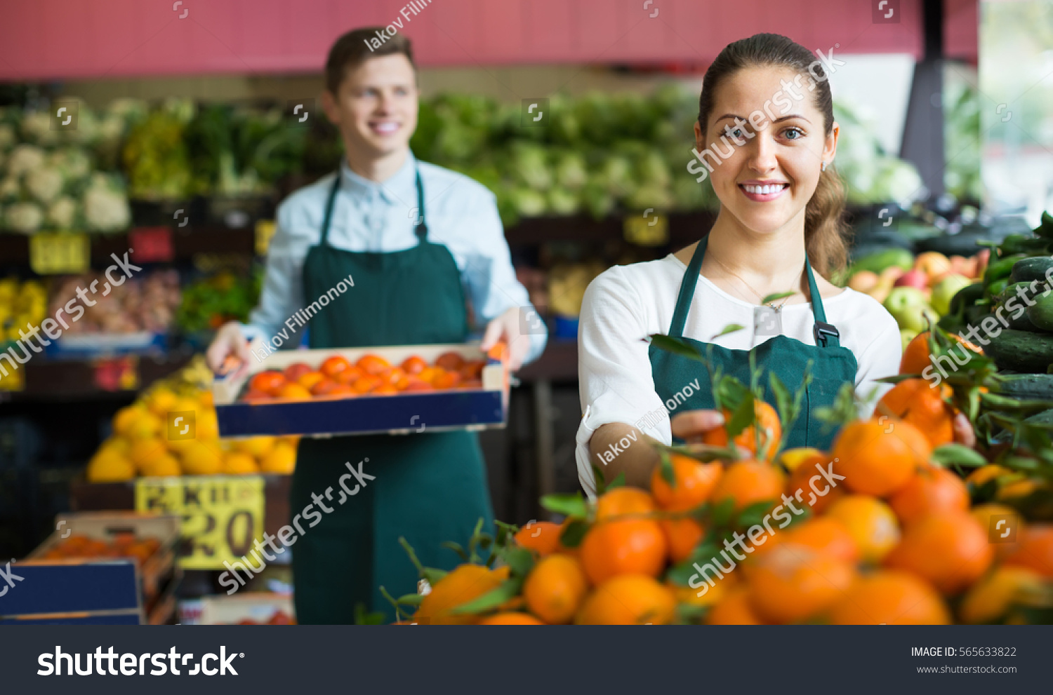 Two smiling supermarket workers in apron arranging citrus in fruit section
